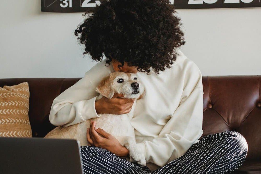 A sad woman hugging a small dog on a sofa